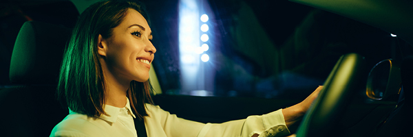 Woman with brown hair smiles while sitting in the driver’s seat with her hands on the wheel.